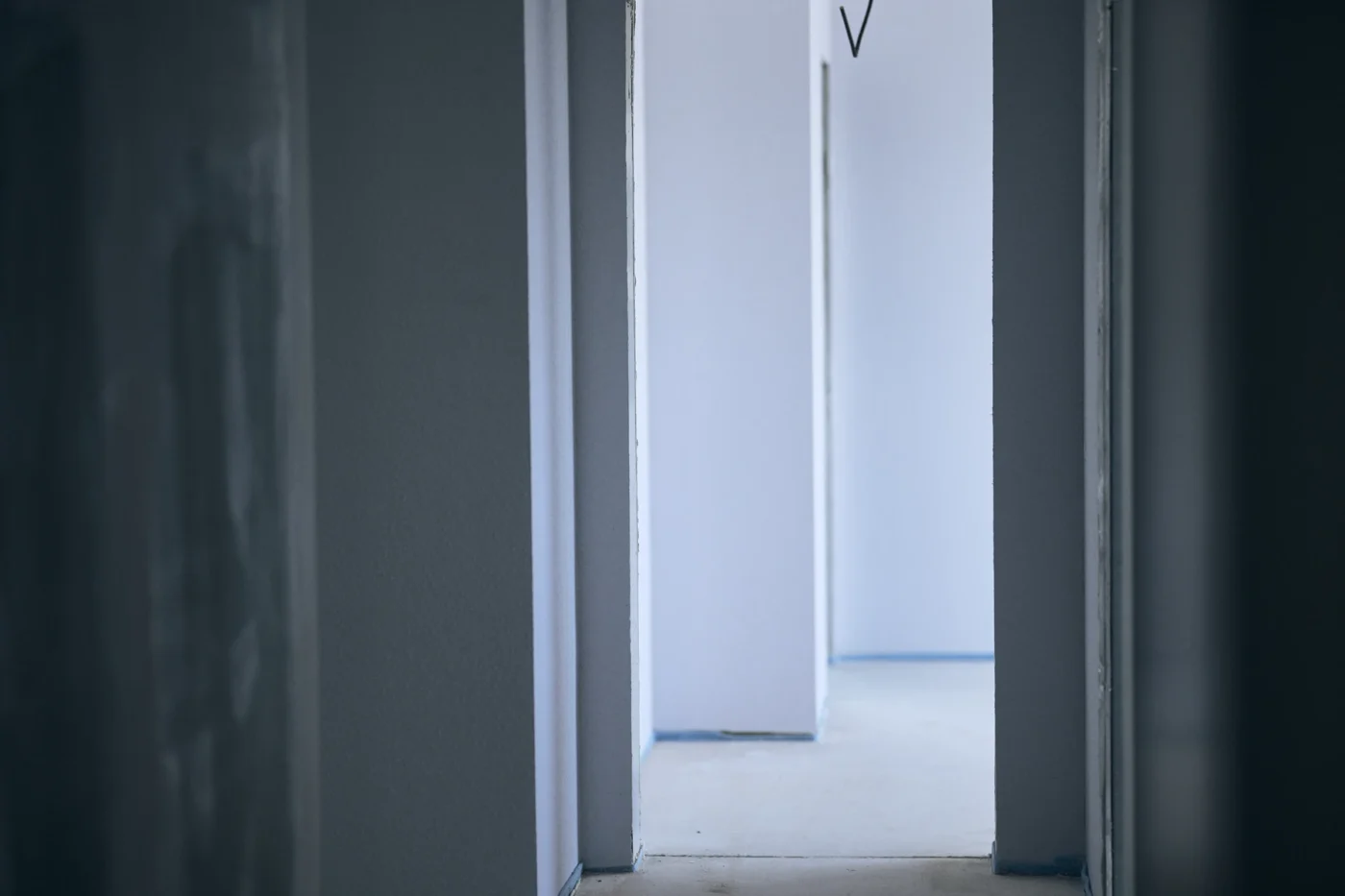 Ein minimalistischer, leerer Flur mit glatten, weißen Wänden und Türöffnungen, der zu einem hell erleuchteten Raum im Hintergrund führt. Der Boden und die Wände wirken sauber, und sanftes Tageslicht durchflutet den Raum.